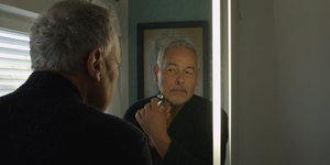 Ein älterer Mann blickt in einen Spiegel und rasiert sich