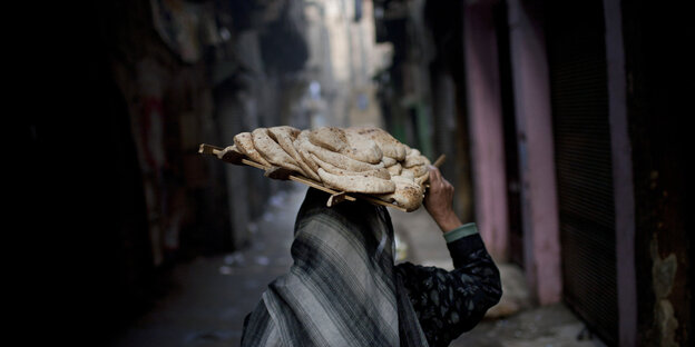 Eine Frau trägt ein Tabeltt mit brot auf dem Kopf