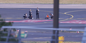 Polizisten stehen auf dem Flugfeld und versuchen Aktivisten der Gruppe Letzte Generation am Flughafen vom Asphalt zu lösen, nachdem diese sich festgeklebt hatten