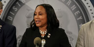 Staatsanwältin Fani Willis spricht in zwei Mikrophone, trägt schwarze Kleindung und hellen Schmuck