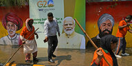 Strassenarbeiterinnen reinigen einen Gehweg nass, dahinter ein Plakat G20 mit dem Gesicht des Premierministers Modi
