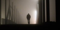 Ein Mann geht am frühen Morgen bei Nebel über eine Brücke