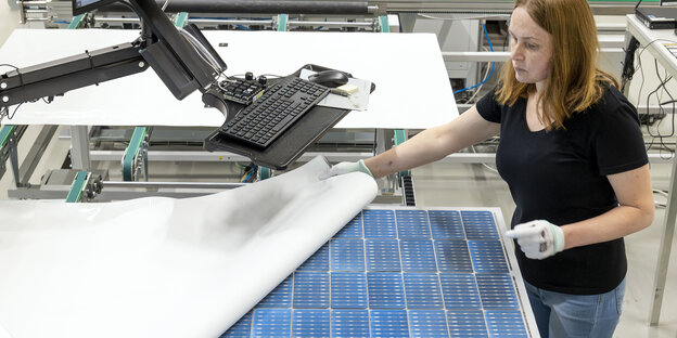 eine Frau mit weißen Handschuhen hebt die Bedeckung von blauen Solarzellen ab
