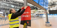 Ein Verdi-Vertreter hängt ein Plakat mit der Aufschrift «WarnStreik» in einem Terminal im Hamburger Flughafen auf.