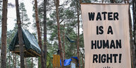 Ein Transparent mit der Aufschrift "Wwater is a human richt" hängt zwischen den Bäumen im Camp von Aktivisten der Initiative "Tesla stoppen" nahe der Tesla-Gigafactory Berlin-Brandenburg.