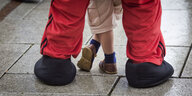 Ein kleines Kind steht zwischen den übergroßen Schuhen eines Mannes.