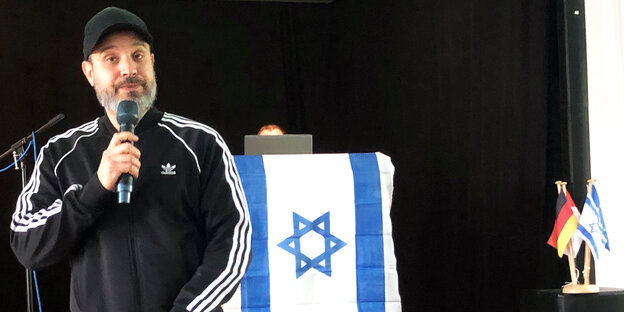 Ben Salomo am Mikrofon mit israelischer Flagge im Hintergrund