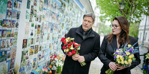 Robert Habeck und Julija Swyrydenko haben Blumen in der Hand und laufen in Kyjiw an einer Mauer entlang