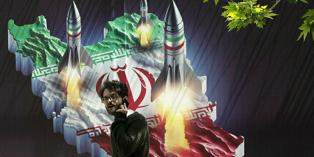 Ein Passant, der mit einem Handy telefoniert, geht an einem Banner vorbei, das Raketen auf der iranischen Landkarte im Norden Teherans zeigt