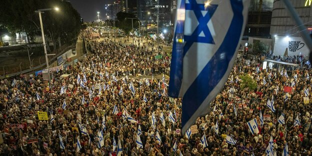 Menschenmasse auf einer israelischen Kreuzung, eine Israelfahne weht darüber