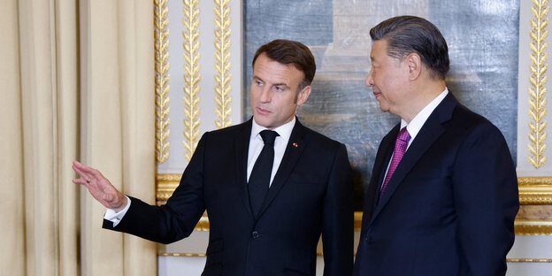 Frankreichs Präsident Macron spricht mit seinem chinesischen Amtskollegen Jinping und weist dabei mit dem Arm in eine bestimmt Richtung