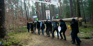 ktivisten tragen in einem Protestcamp einen Baumstamm im Wald. Das Protestcamp richtet sich gegen eine geplante Erweiterung des Tesla-Werksgeländes in einem Waldgebiet nahe der Fabrik.